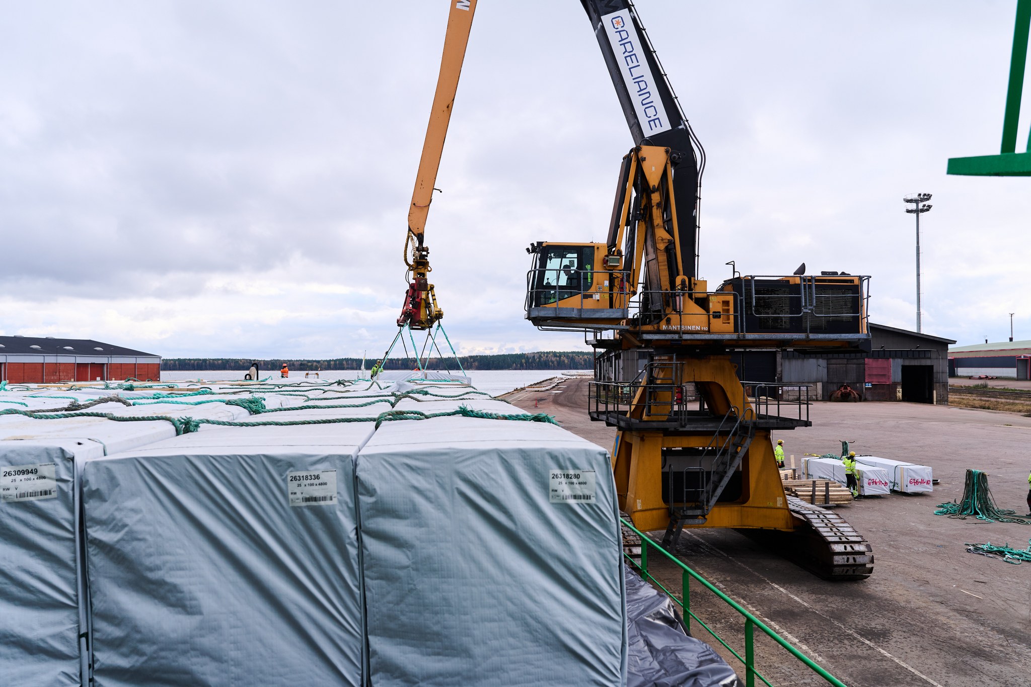A material handling machine lifts a load of sawn timber beside a vessel.