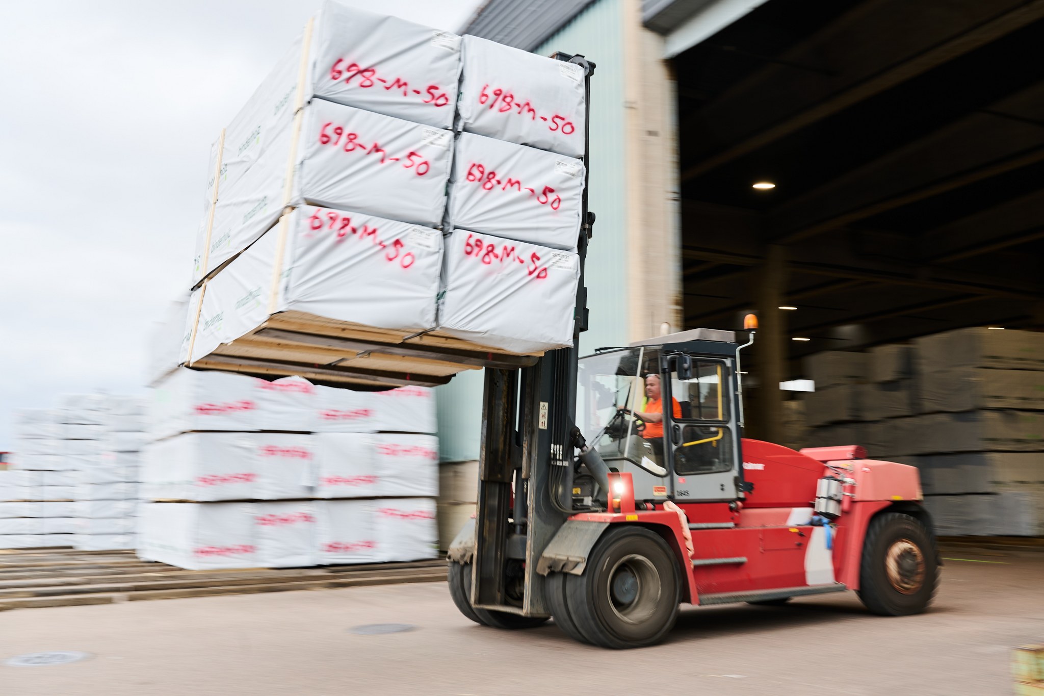 A forklift moves packaged sawn timber in front of a warehouse building.